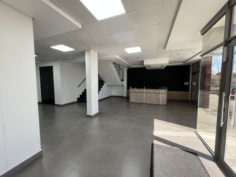 Spacious office entrance area featuring a built-in reception desk, modern tiled flooring, recessed ceiling lighting, and a staircase leading to the upper level.