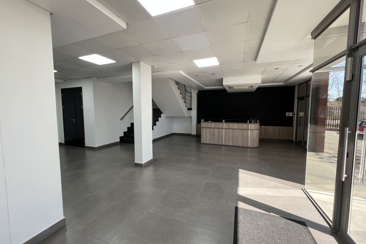 Spacious office entrance area featuring a built-in reception desk, modern tiled flooring, recessed ceiling lighting, and a staircase leading to the upper level.