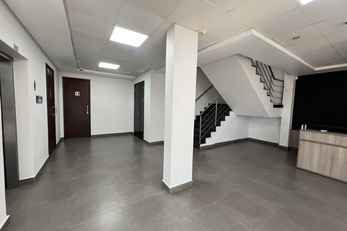 Spacious office lobby featuring tiled flooring, a central staircase with metal railings, elevator access, and a built-in reception desk.