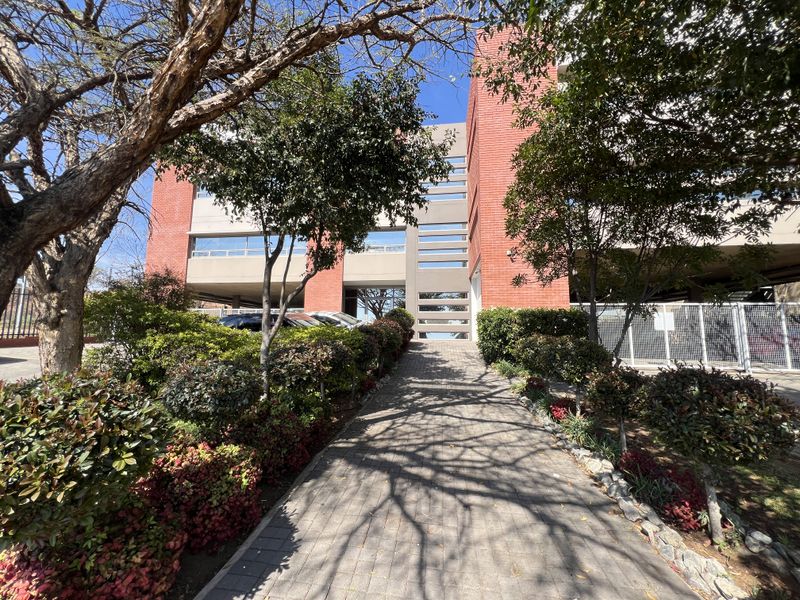 A well-maintained office building exterior featuring a red brick facade, a paved pedestrian walkway, and established garden landscaping.
