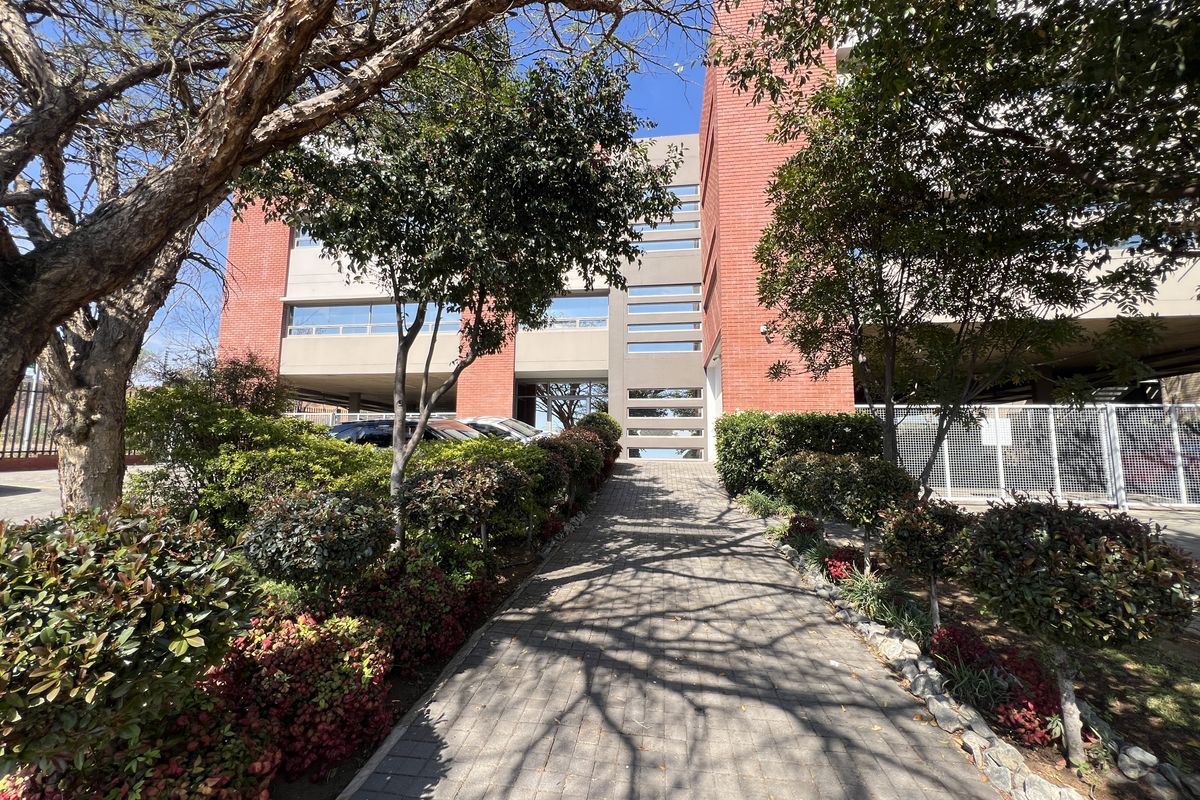 A well-maintained office building exterior featuring a red brick facade, a paved pedestrian walkway, and established garden landscaping.