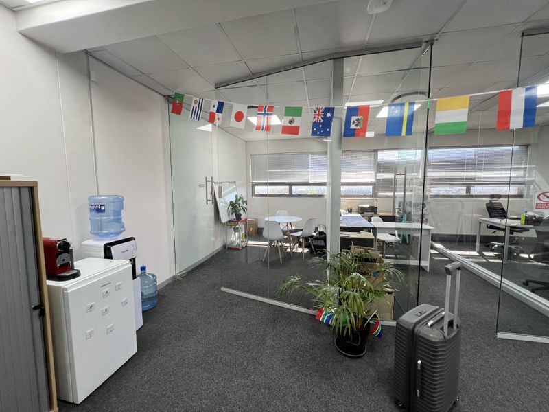 A modern office space featuring glass partition walls, suspended ceilings, and carpeted flooring, providing a professional and bright working environment.