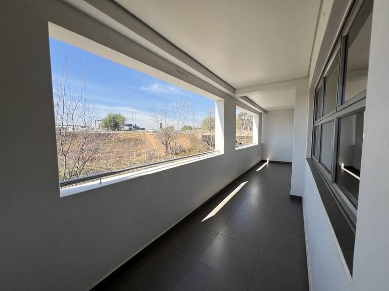 A clean, modern covered balcony featuring tiled flooring and a metal balustrade, offering an open view of the surrounding area.