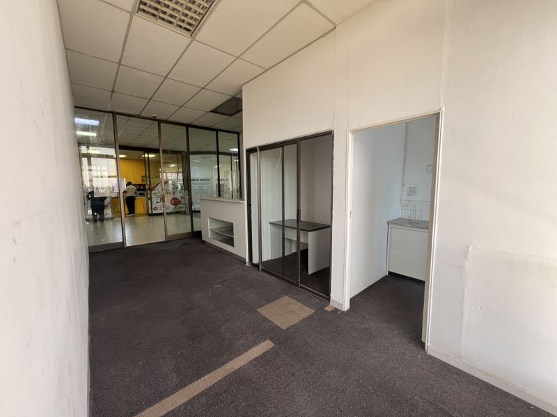 A vacant commercial utility space featuring glass partitions, a built-in reception counter, and a small kitchenette area with basic cabinetry.