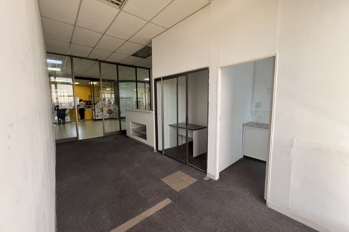 A vacant commercial utility space featuring glass partitions, a built-in reception counter, and a small kitchenette area with basic cabinetry.