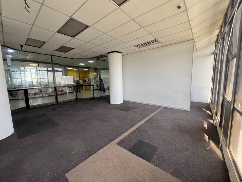 Empty open-plan retail space featuring suspended ceilings, structural columns, glass partitioning, and carpeted flooring, suitable for various commercial business layouts.