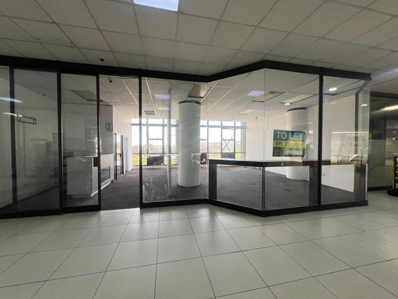 An open-plan commercial retail space featuring glass partitioning, suspended ceilings, and large windows, currently vacant and available for lease.