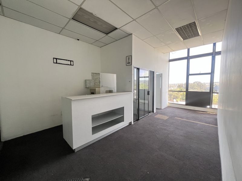 Empty office space featuring a built-in reception desk, large windows with natural light, and a suspended ceiling with recessed lighting.