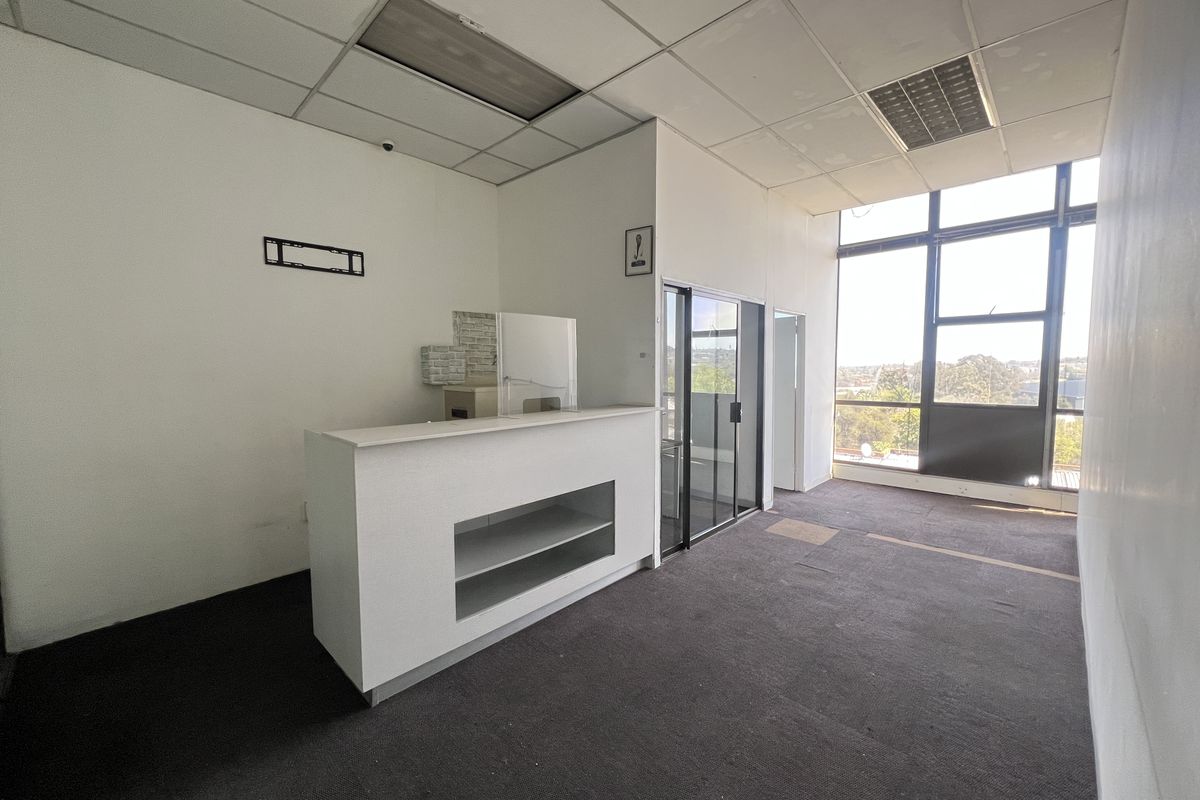 Empty office space featuring a built-in reception desk, large windows with natural light, and a suspended ceiling with recessed lighting.