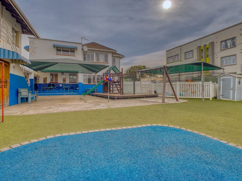Rear exterior area featuring a paved patio, artificial turf, shade sails, and a dedicated play space with fencing.