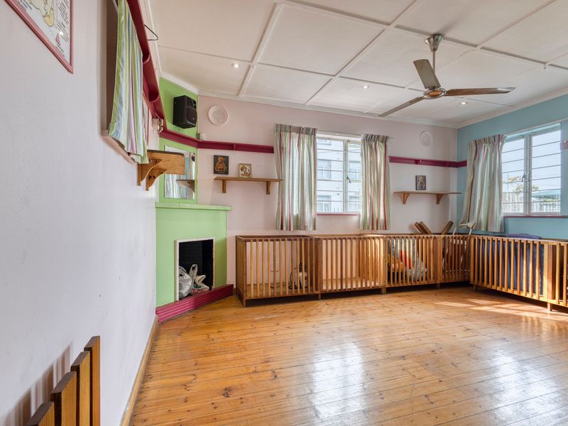 Spacious room featuring original timber flooring, a fireplace, ceiling fan, and large windows with security bars, offering a versatile layout for commercial use.
