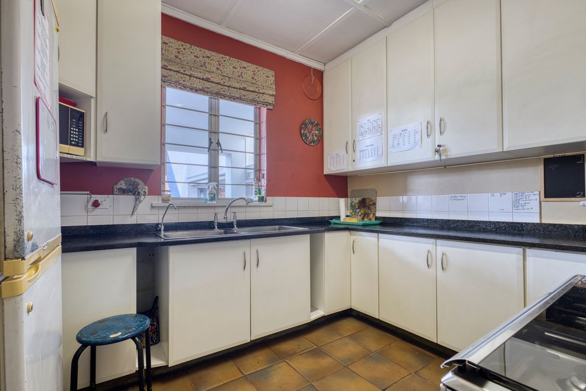 A functional kitchen featuring white built-in cabinetry, dark laminate countertops, a double basin sink, and tiled flooring with a red accent wall.