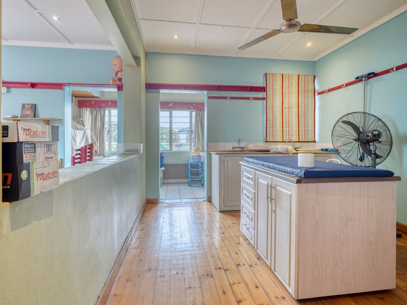 A functional utility space featuring timber flooring, built-in cabinetry with a sink, and a ceiling fan, offering practical workspace for commercial operations.