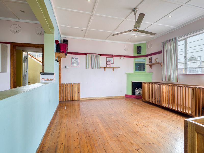 Spacious living area featuring original hardwood flooring, a built-in fireplace, and a coffered ceiling with a central fan, offering a versatile commercial space.