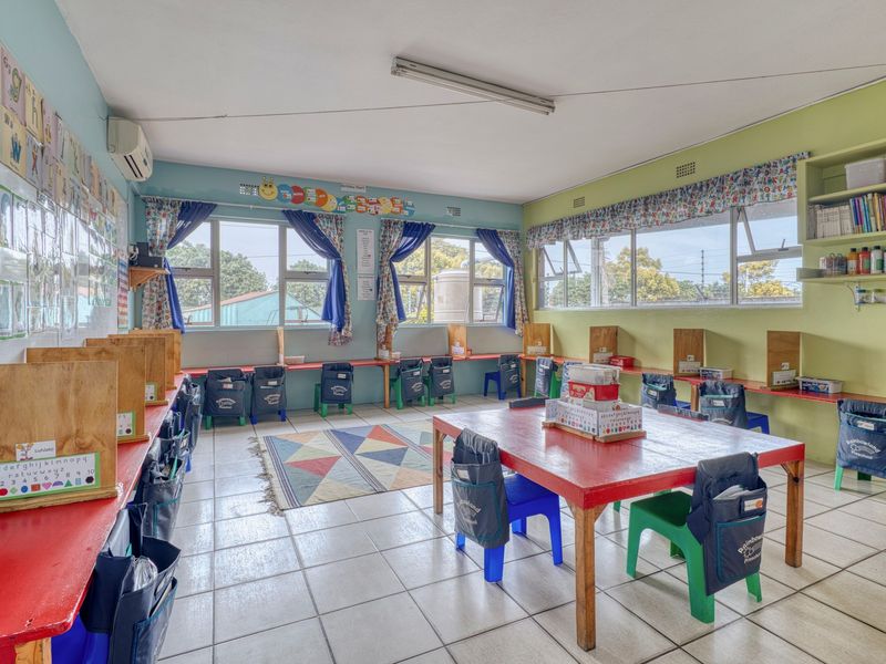 A functional classroom space featuring tiled flooring, built-in shelving, and large windows providing natural light, suitable for educational or commercial use.