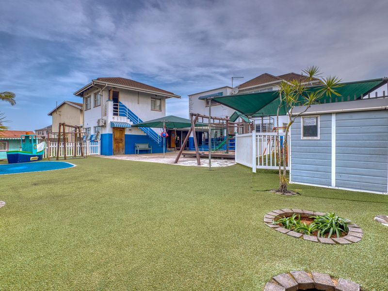 Spacious rear outdoor area featuring artificial turf, paved patio space, shade sails, and a storage shed, suitable for commercial or recreational use.