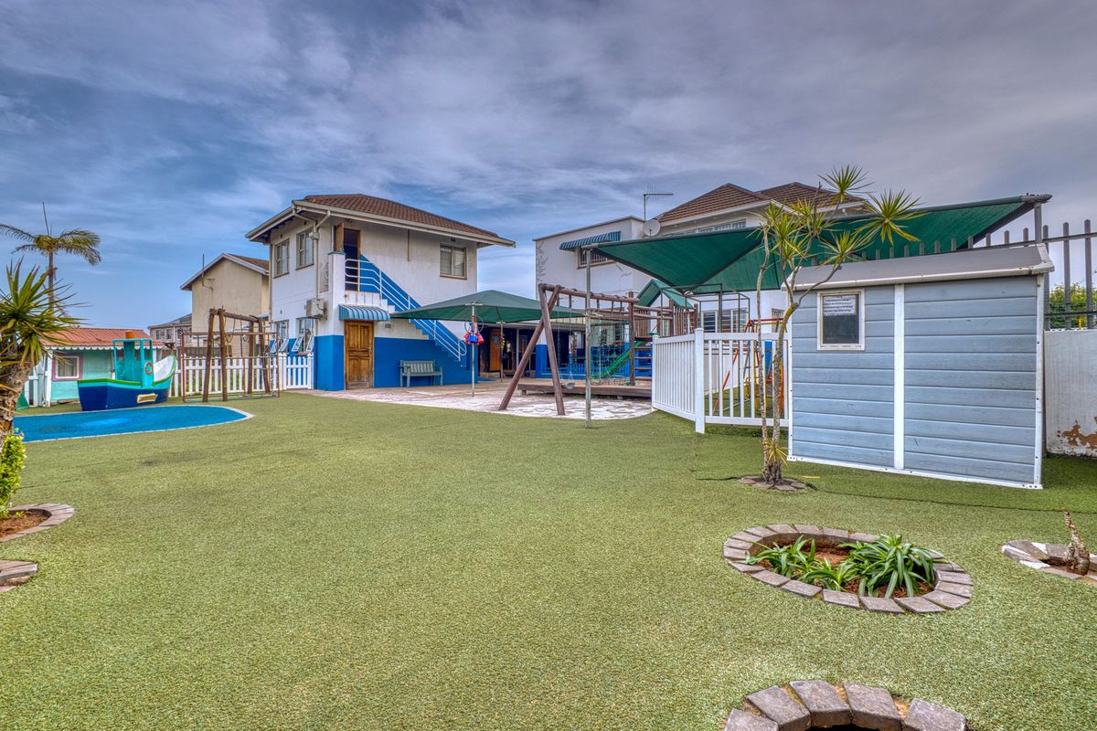 Spacious rear outdoor area featuring artificial turf, paved patio space, shade sails, and a storage shed, suitable for commercial or recreational use.