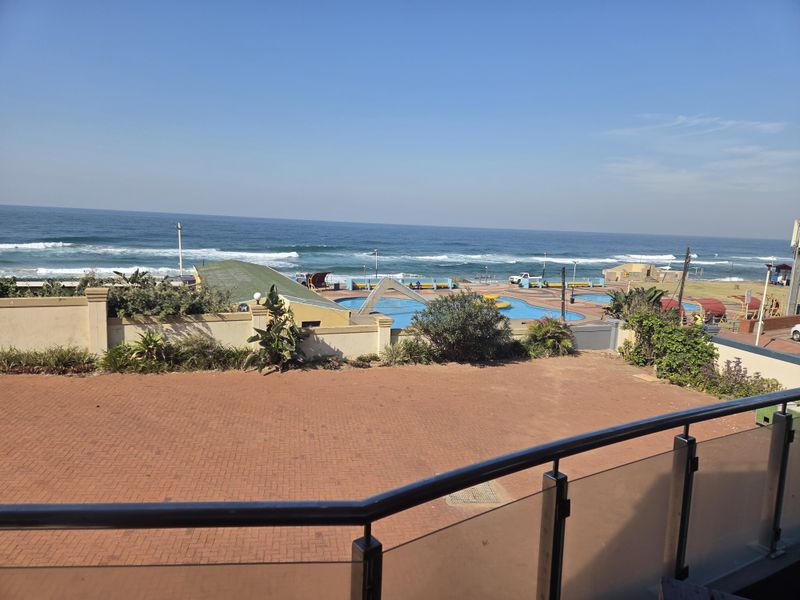 Elevated view overlooking a paved terrace, boundary wall, and coastal pool area with direct ocean views.