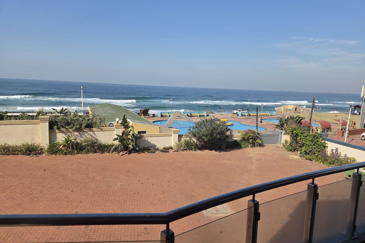 Elevated view overlooking a paved terrace, boundary wall, and coastal pool area with direct ocean views.