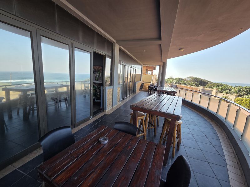 Spacious covered balcony terrace featuring tiled flooring, glass balustrades, and expansive ocean views, ideal for outdoor dining and restaurant seating.