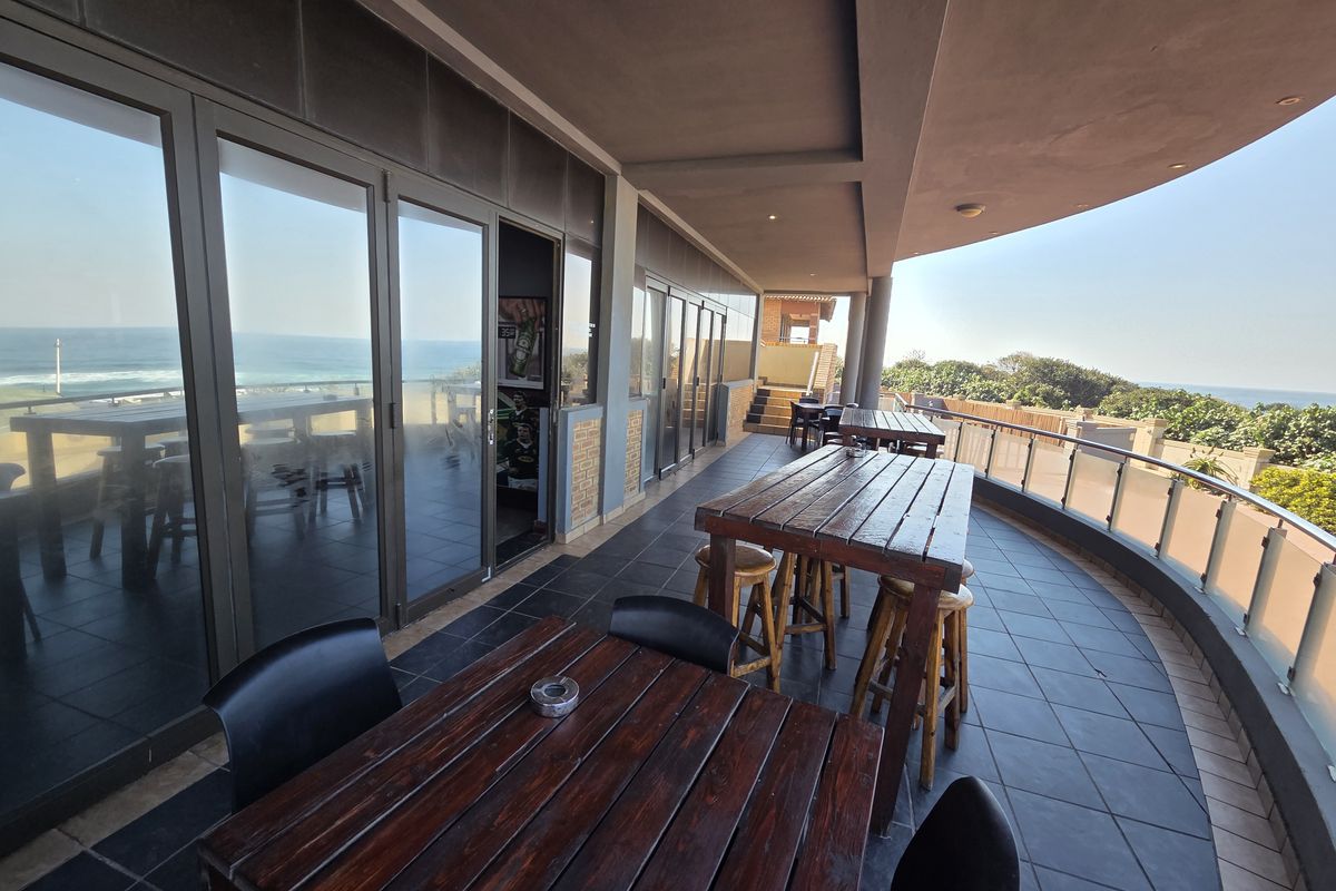 Spacious covered balcony terrace featuring tiled flooring, glass balustrades, and expansive ocean views, ideal for outdoor dining and restaurant seating.