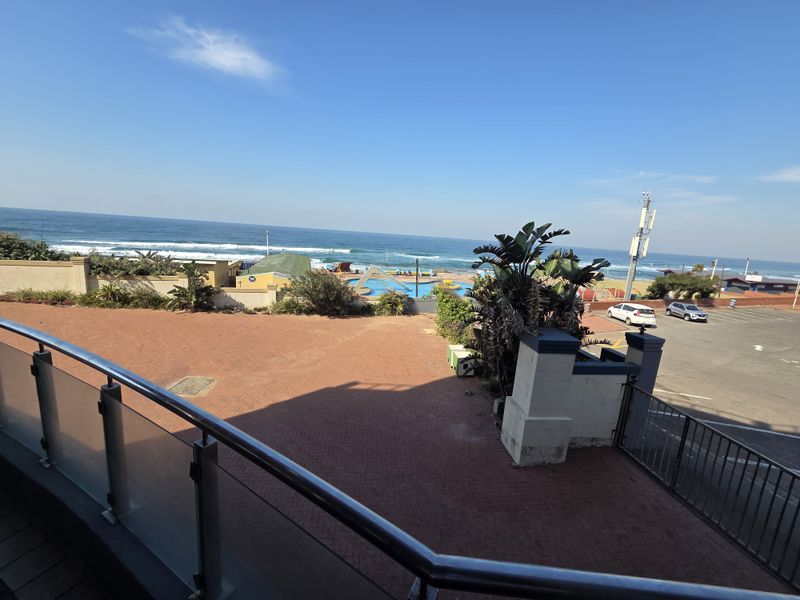 Elevated view overlooking a paved courtyard, perimeter wall, and coastal scenery with ocean views.