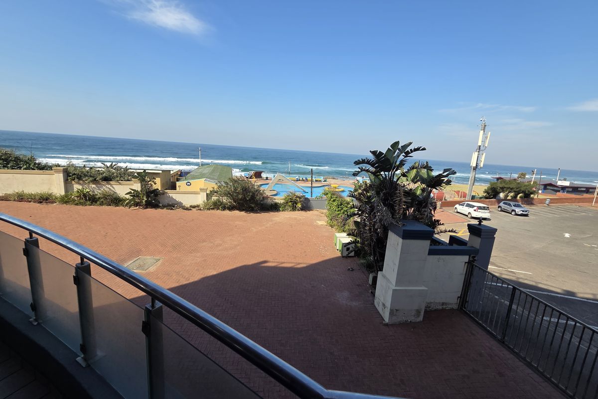 Elevated view overlooking a paved courtyard, perimeter wall, and coastal scenery with ocean views.