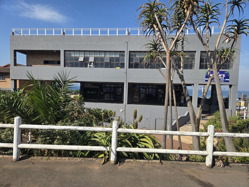 A multi-level commercial restaurant building featuring a modern grey concrete facade, large steel-framed windows, and an open-air ground level entrance.