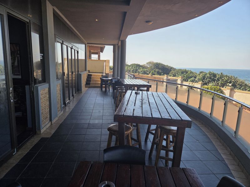 Spacious covered balcony featuring dark tiled flooring, a modern glass balustrade, and expansive ocean views, ideal for outdoor dining and relaxation.