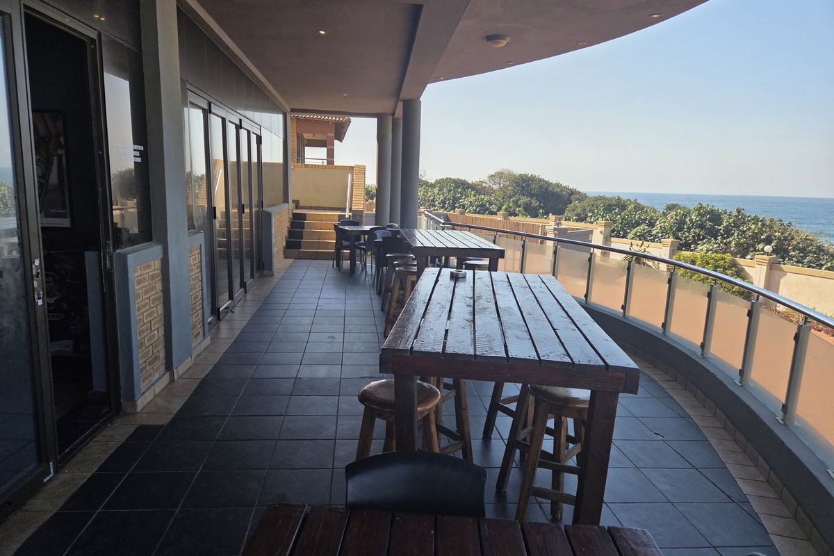 Spacious covered balcony featuring dark tiled flooring, a modern glass balustrade, and expansive ocean views, ideal for outdoor dining and relaxation.
