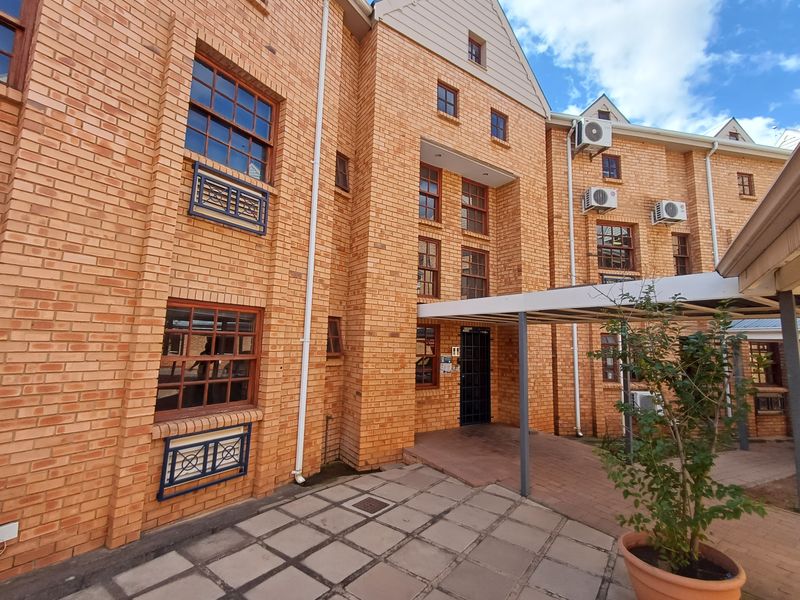 Exterior view of a multi-story office building featuring face brick construction, timber framed windows, and a paved courtyard with a covered walkway.