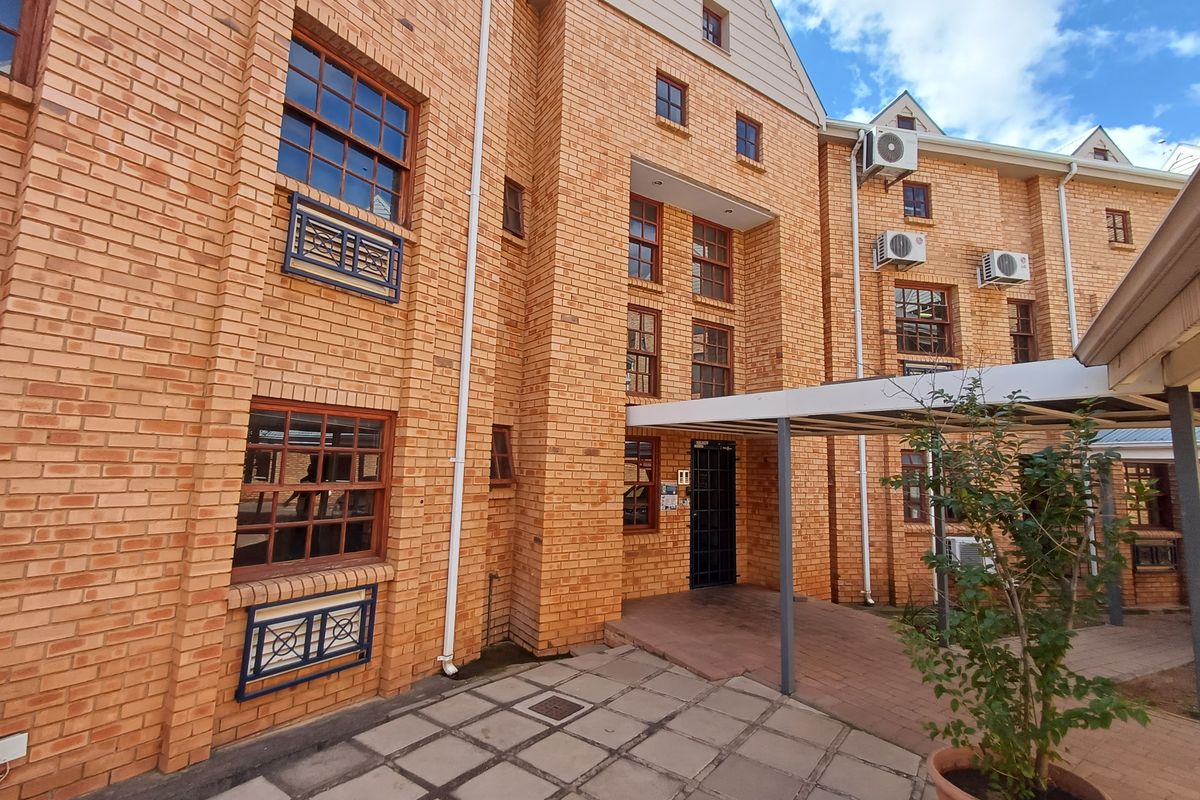 Exterior view of a multi-story office building featuring face brick construction, timber framed windows, and a paved courtyard with a covered walkway.