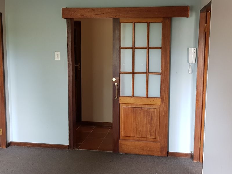 An empty office space featuring a sliding wooden door, intercom system, and neutral wall finishes, suitable for a professional workspace.