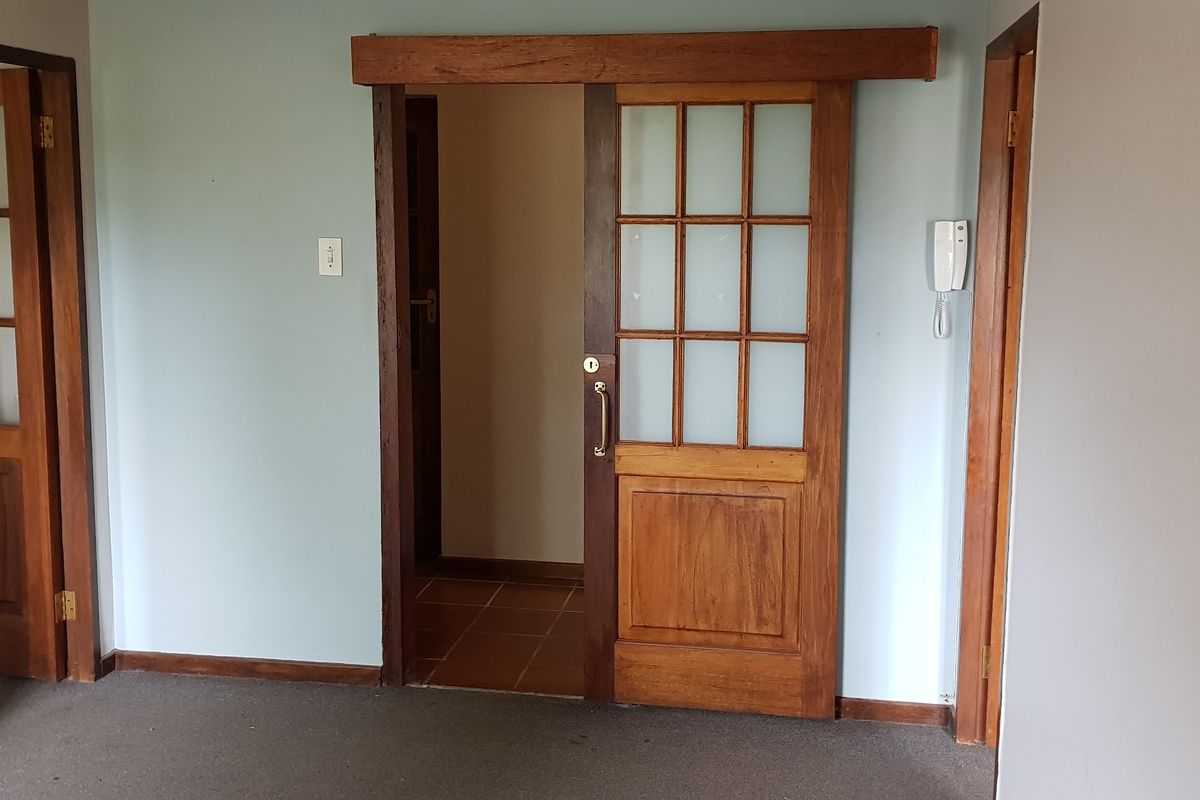 An empty office space featuring a sliding wooden door, intercom system, and neutral wall finishes, suitable for a professional workspace.