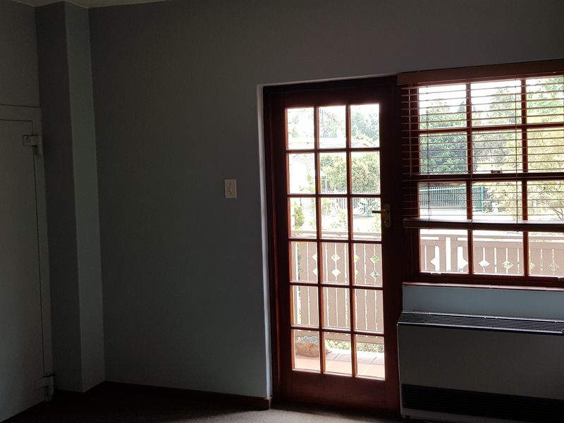 An empty office space featuring a secure door, large window with venetian blinds, and a built-in HVAC unit.