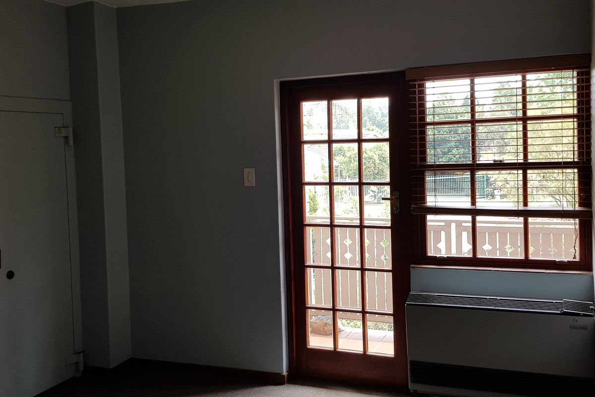 An empty office space featuring a secure door, large window with venetian blinds, and a built-in HVAC unit.