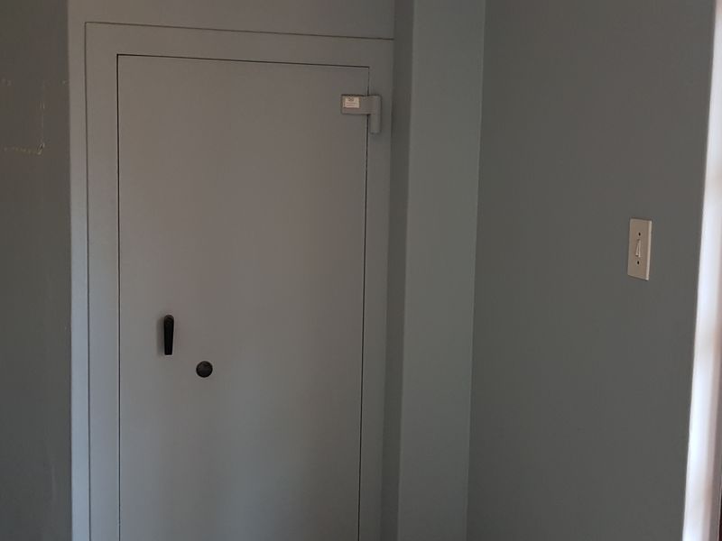 An office space featuring a secure built-in safe, neutral wall finishes, and a timber-framed glass door providing natural light.