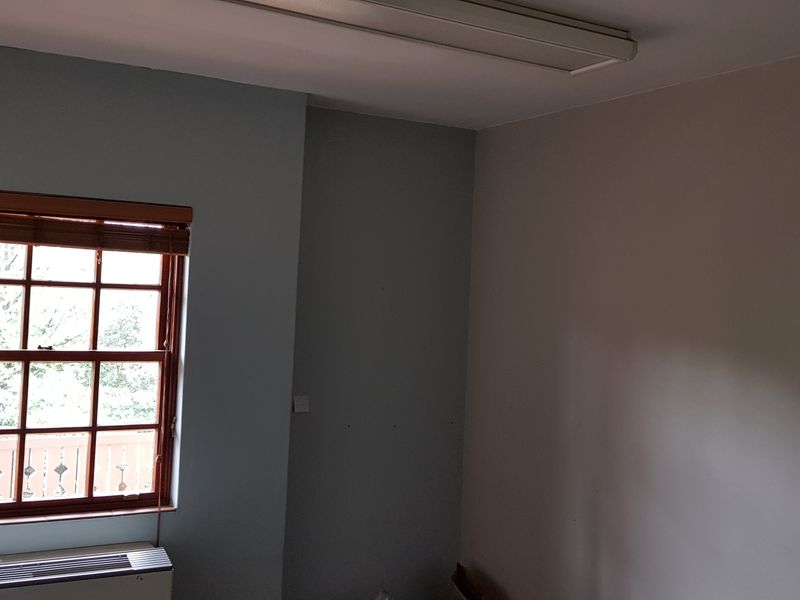 A vacant office space featuring a timber sash window with integrated blind, wall-mounted HVAC unit, and overhead fluorescent lighting.