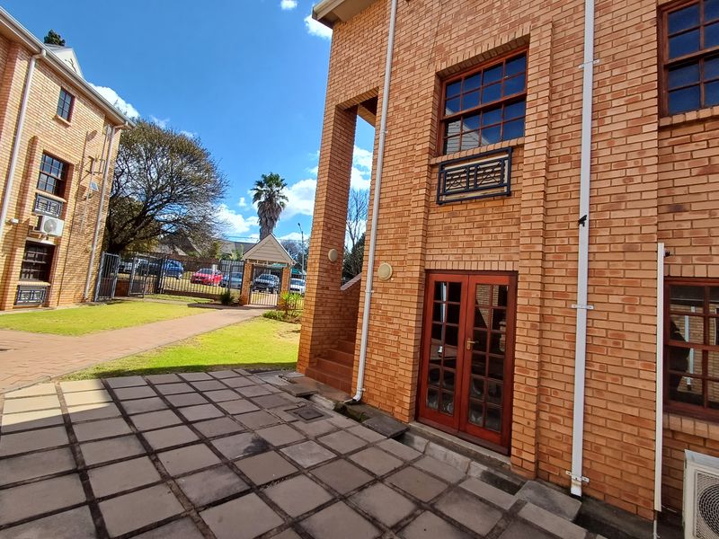 Rear view of a face brick office building featuring a paved patio area, timber-framed glass doors, and well-maintained exterior brickwork.