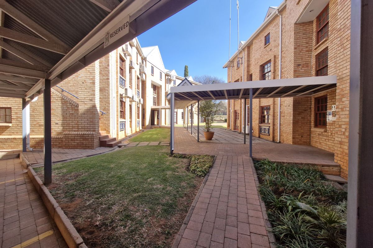 A well-maintained office complex courtyard featuring brick facades, covered walkways, paved paths, and landscaped garden areas between the building wings.