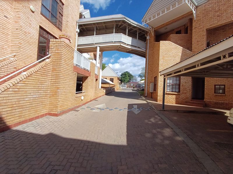 Exterior view of an office complex featuring brick architecture, a connecting pedestrian bridge, and a paved driveway with covered parking.