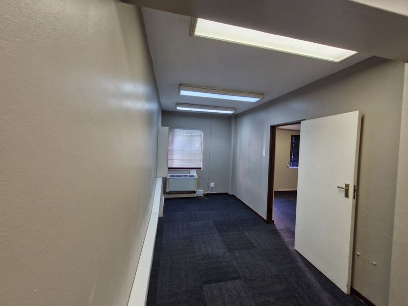 A vacant office space featuring carpeted flooring, fluorescent ceiling lighting, and a wall-mounted air conditioning unit.