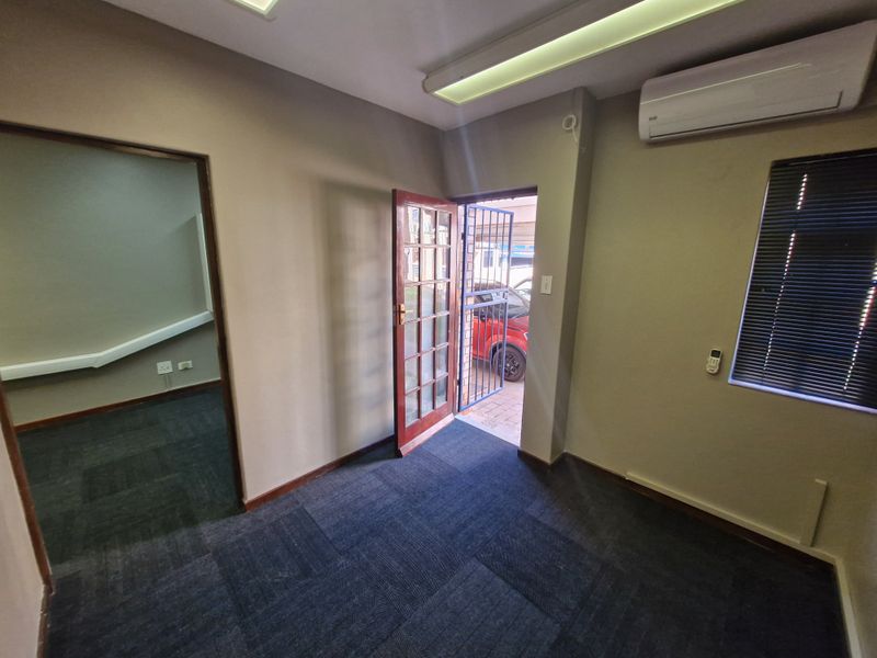 A vacant office space featuring carpet tiles, air conditioning, and direct exterior access through a security gate and timber door.