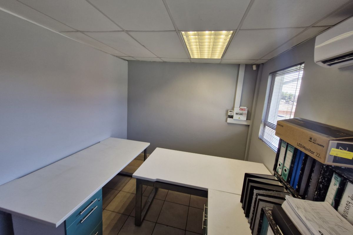 A functional office space featuring tiled flooring, a suspended ceiling with recessed lighting, and a wall-mounted air conditioning unit.