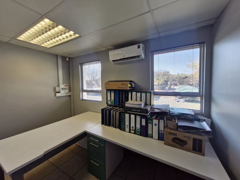 A functional office space featuring a built-in desk, split-system air conditioning, recessed ceiling lighting, and large windows with venetian blinds.