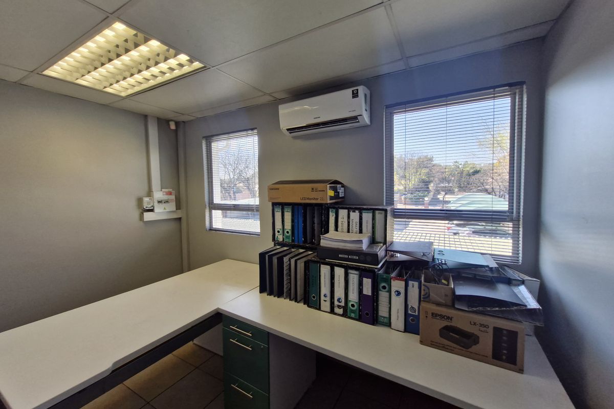 A functional office space featuring a built-in desk, split-system air conditioning, recessed ceiling lighting, and large windows with venetian blinds.