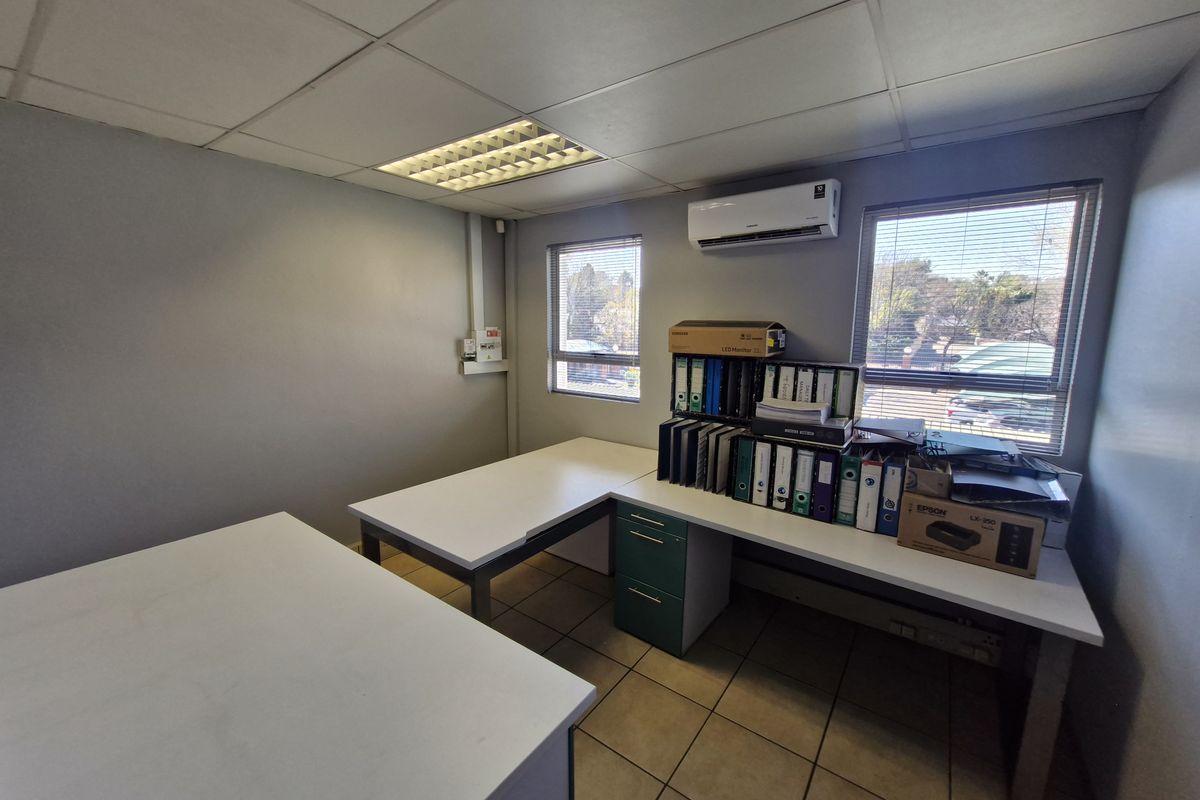 A functional office space featuring tiled flooring, a suspended ceiling with recessed lighting, and a wall-mounted air conditioning unit.