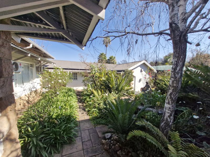 A well-maintained rear garden area featuring a paved walkway, lush established greenery, and views of the office building exterior.