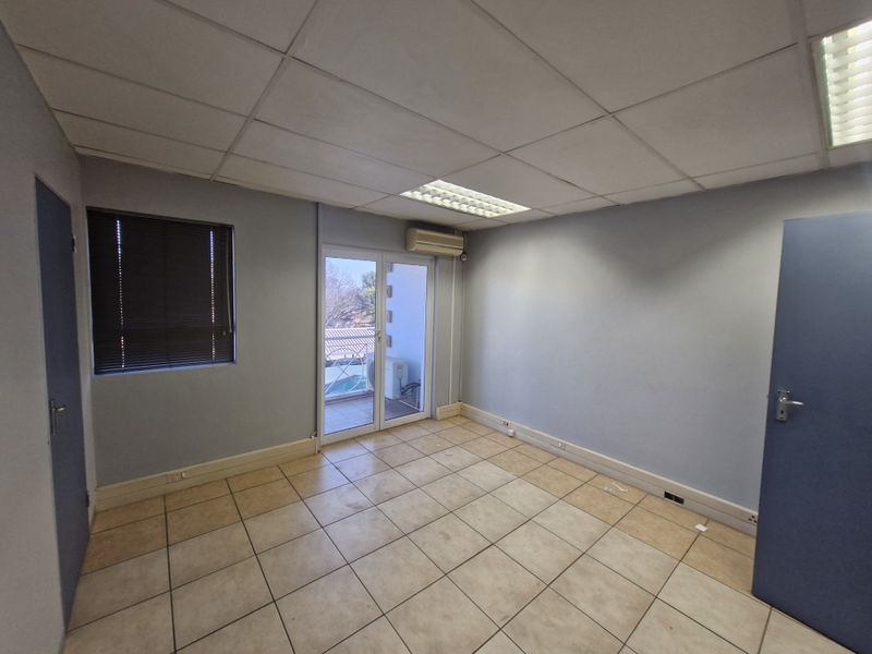 A vacant office space featuring ceramic tile flooring, a suspended ceiling with recessed lighting, and a glass door leading to a small balcony.