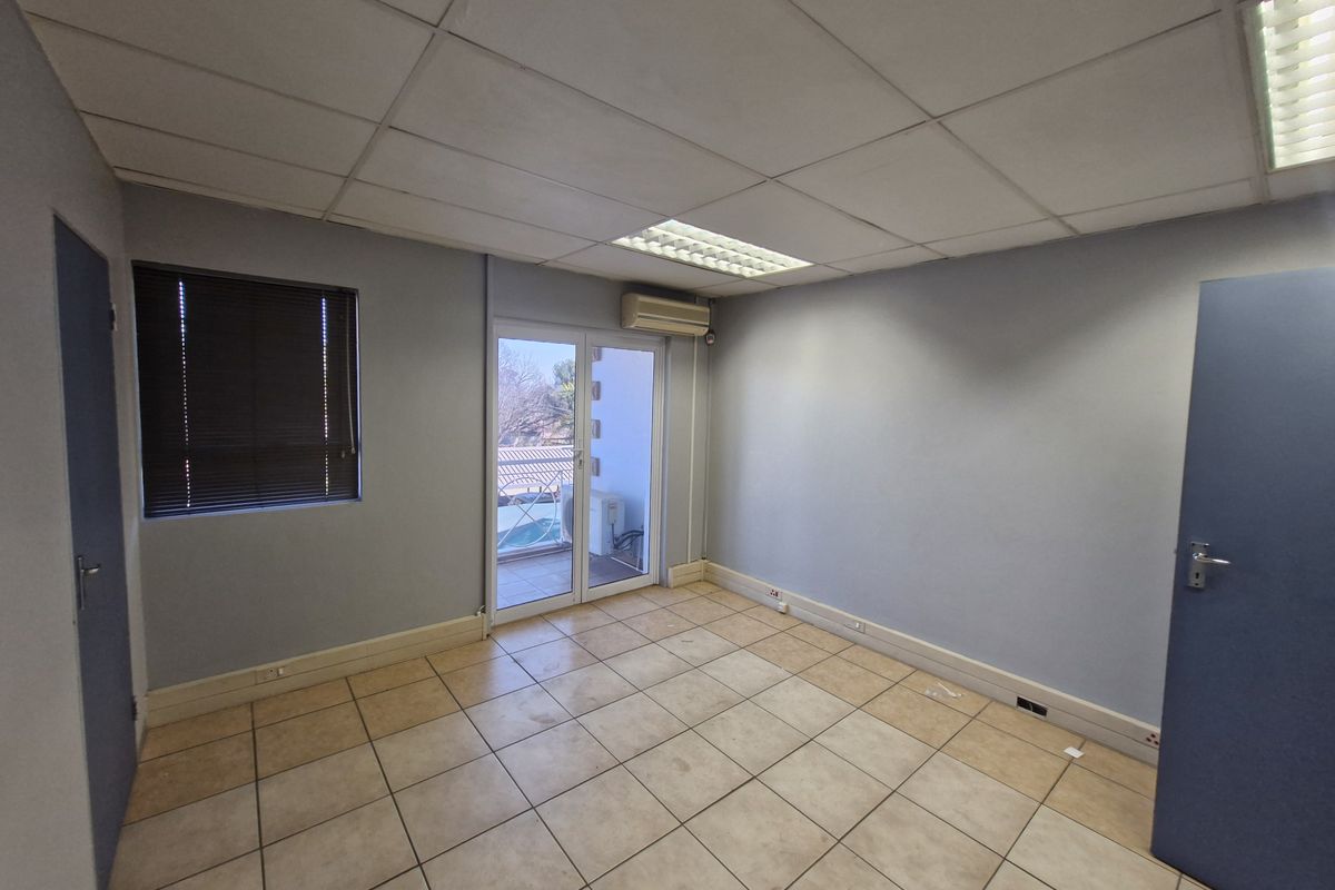 A vacant office space featuring ceramic tile flooring, a suspended ceiling with recessed lighting, and a glass door leading to a small balcony.